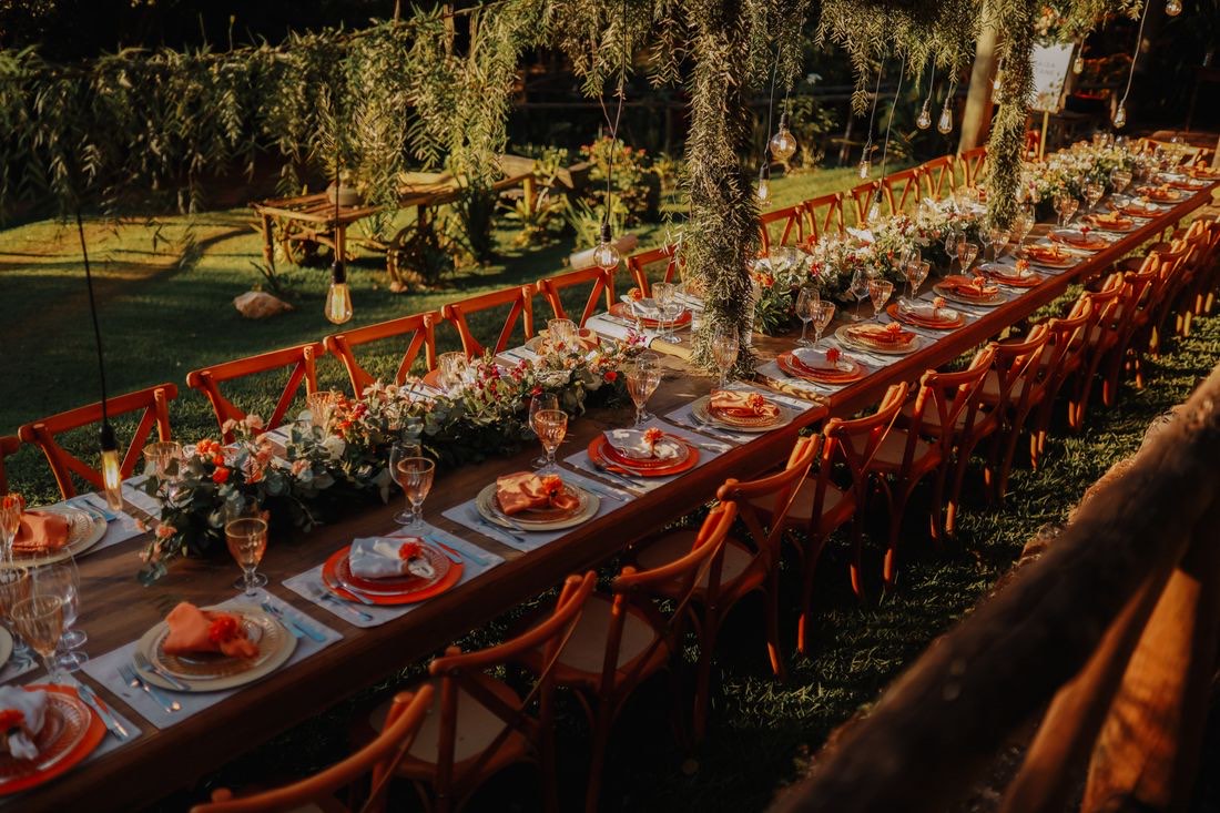 Mesas compridas decoradas num jardim com árvores